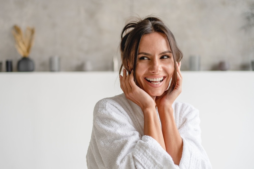 Femme à la peau saine et lumineuse, souriant joyeusement dans son peignoir, idéale pour illustrer les bienfaits des soins de la peau avec des produits tels que l'aloe vera.